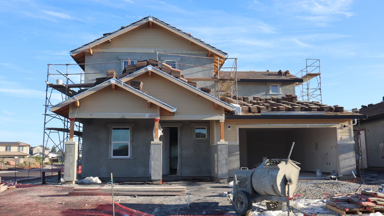 Front view of a modern two-story house under construction in a suburban neighborhood.