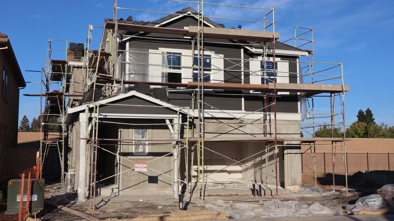 A two-story house under construction, surrounded by scaffolding on a clear, sunny day.
